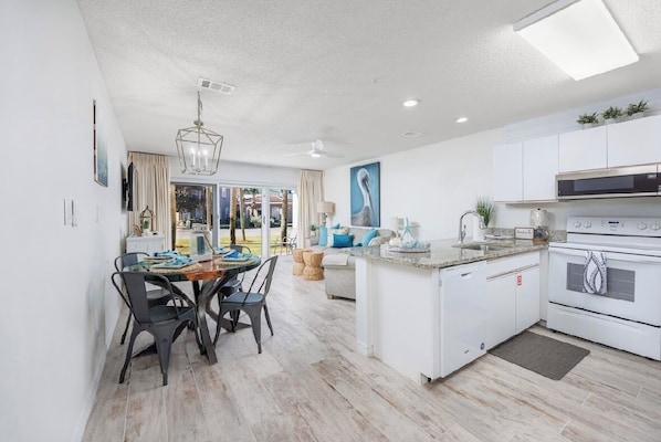 A modern kitchen with white cabinets, a built-in oven, and a dining area with a round table and chairs.