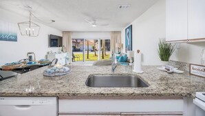 A modern kitchen with granite countertops, a stainless steel sink, and a dining area with a view of the outdoors. - 🏖️ 5⭐️ Maravilla 4108!☀️Beautiful Remodel! 1 Bd 1.5 Bath w Bunks-Beach Svc 2Pools! (Miramar Beach)