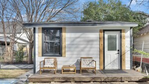 A small house with a porch, two chairs, and a small table.