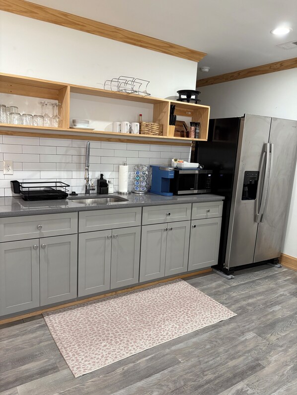 Una cocina moderna con armarios grises, un refrigerador de acero inoxidable, una cafetera y un microondas.
