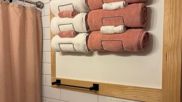 A bathroom with a towel rack holding neatly folded towels, a shower curtain, and a wooden panel above the tiles.