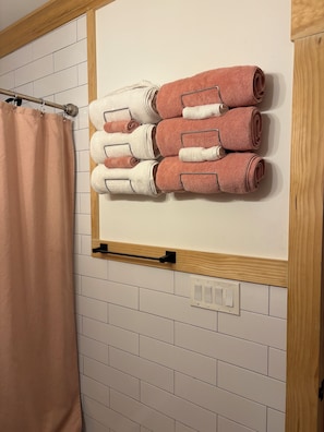 Un baño con un perchero que sostiene toallas dobladas con cuidado, una cortina de ducha y un panel de madera sobre los azulejos.