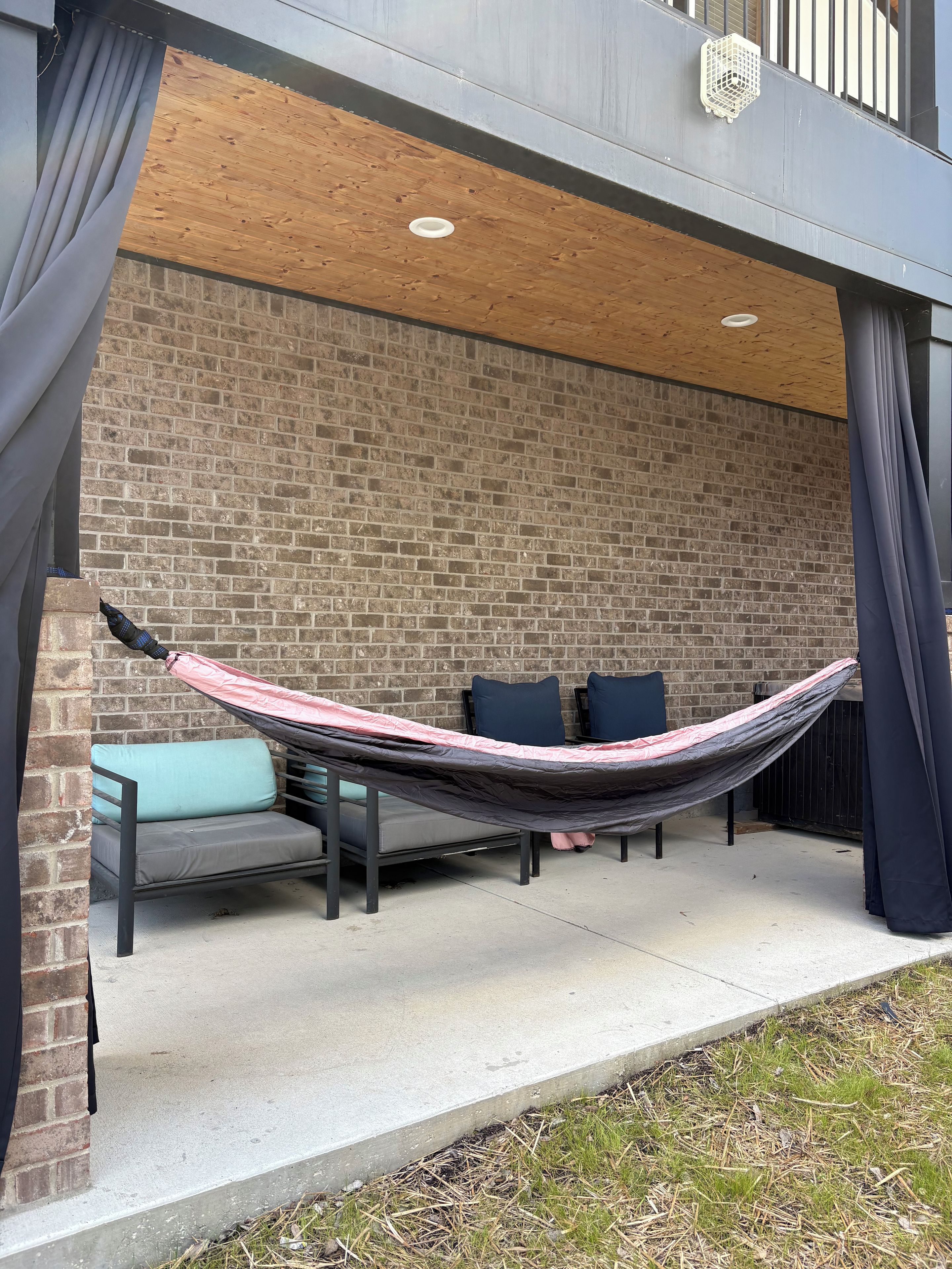 An outdoor seating area with a hammock, a cushioned bench, and a brick wall backdrop.