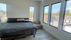 A bedroom with a bed, a ceiling fan, and large windows offering a view of the neighborhood. - 1 mile to Downtown St Petersburg new construction luxury 2,155 sqft home (St. Petersburg)