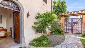 A stone pathway leading to a wooden door with a metal gate, surrounded by greenery and a small tree. - Chianti Classico Home Panoramic View 4, Castellina in Chianti, Italy (Castellina in Chianti)