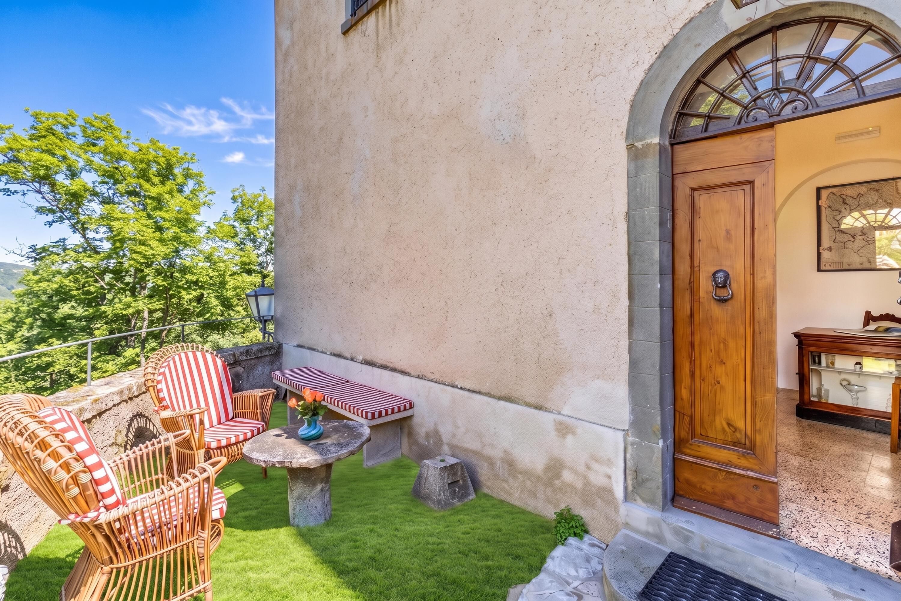 Eine Terrasse mit Korbmöbeln und einem kleinen Tisch, eine Holztür mit einer Karte sowie ein Blick auf Bäume.