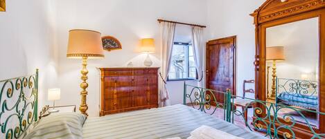 A room with a bed, two bedside lamps, a dresser, a mirror, and a window with curtains.