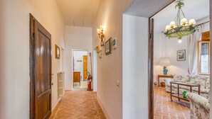 A hallway with a wooden door, a fire extinguisher, and a sofa with a floral pattern. - Chianti Classico Home Panoramic View 6, Castellina in Chianti, Italy (Castellina in Chianti)