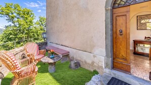 A patio with wicker furniture and a small table, a wooden door with a map, and a view of trees. - Chianti Classico Home Panoramic View 6, Castellina in Chianti, Italy (Castellina in Chianti)