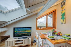 A dining area with a wooden table, chairs, a TV, and a window with a view of the outdoors.