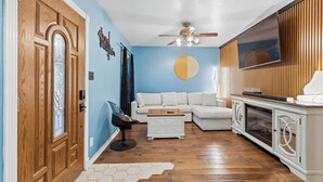 A living room with a wooden door, a white sofa, a coffee table, and a TV on a wooden cabinet.