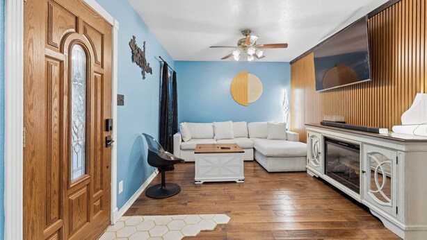 Una sala de estar con puerta de madera, un sofá blanco, una mesa de centro y un televisor sobre un mueble de madera.