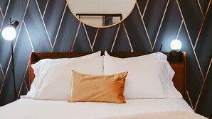 Una cama con ropa de cama blanca y marrón, un espejo redondo encima y dos lámparas de noche.