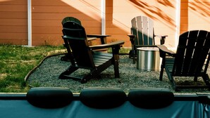 Un jacuzzi con tres sillas Adirondack y una mesa, rodeado por una valla de madera y follaje.