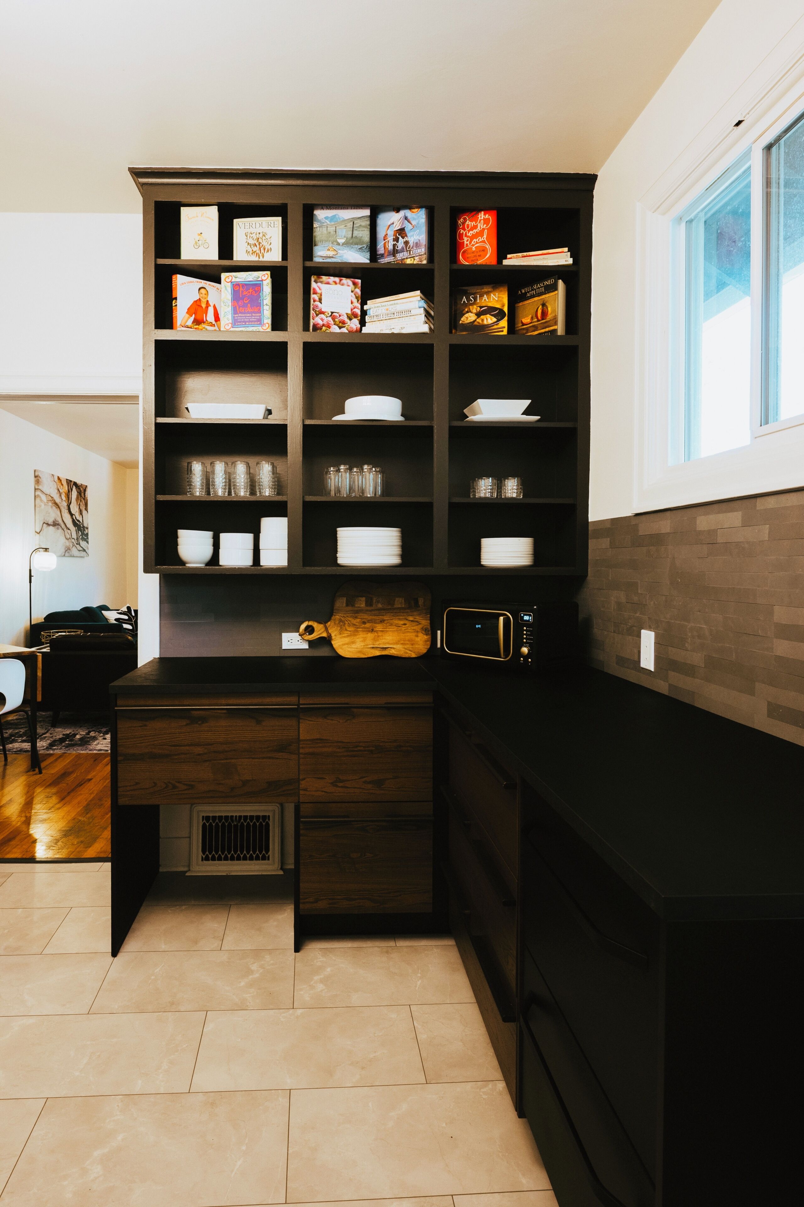 Una cocina con una estantería empotrada, un microondas y una ventana.