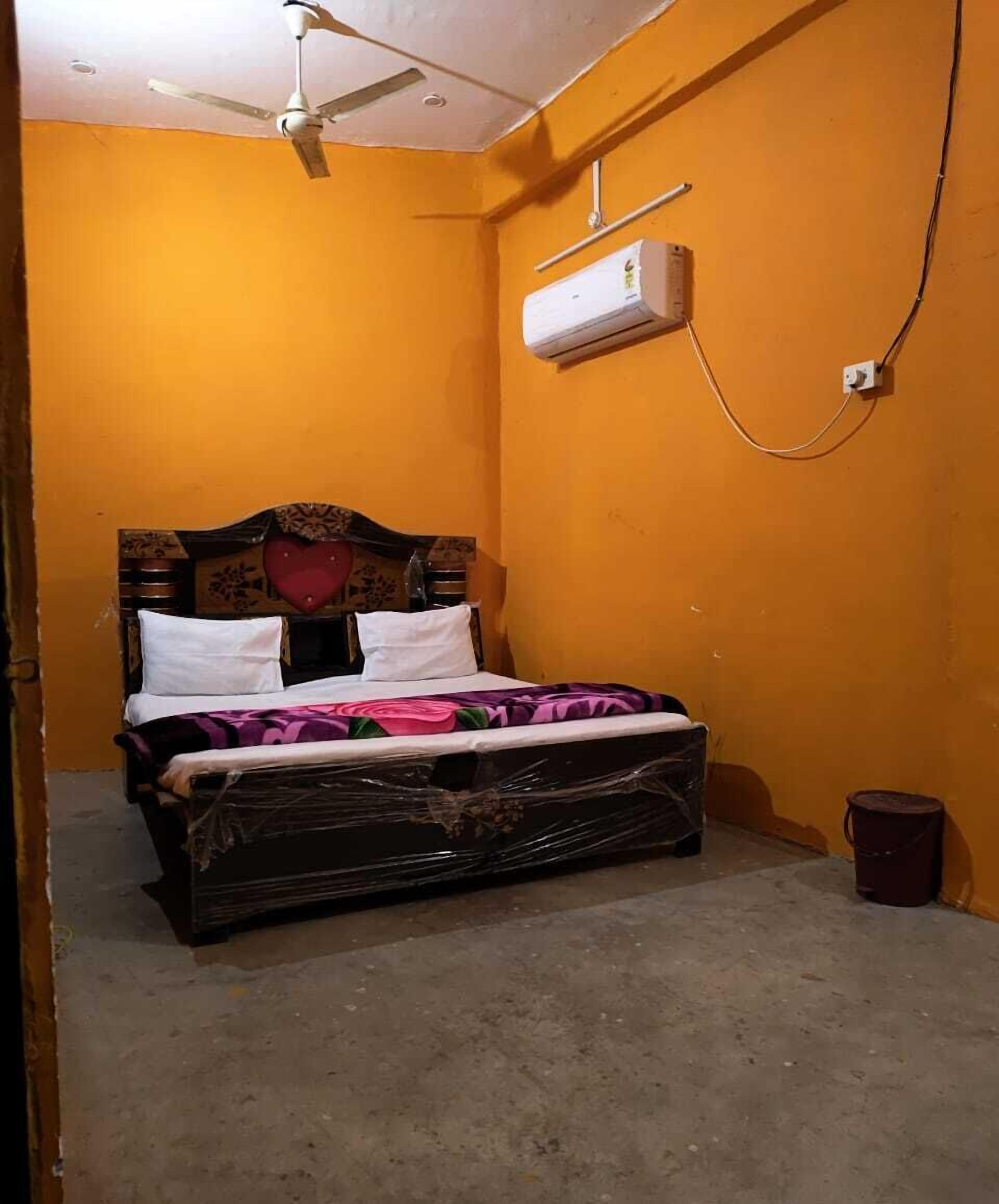 A single bed with a wooden headboard, a red heart decoration, and a floral-patterned blanket. An air conditioning unit is mounted on the wall above the bed.