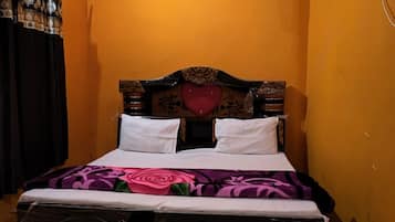 A single bed with a wooden headboard and a heart-shaped decoration, a white air conditioner on the wall, and a ceiling fan.