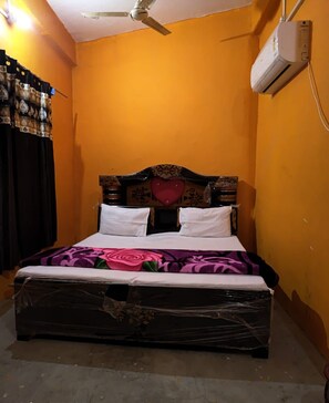 A single bed with a wooden headboard and a heart-shaped decoration, a white air conditioner on the wall, and a ceiling fan. - Hotel Diamond Hardoi (Bilgram)