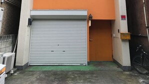 A two-story building with a closed garage door, a small balcony on the upper floor, and a bicycle parked outside. - 2min walk from Nakano Station 1min walk to Nakano Broadway MAX4 Guests(2) (中野区中野)