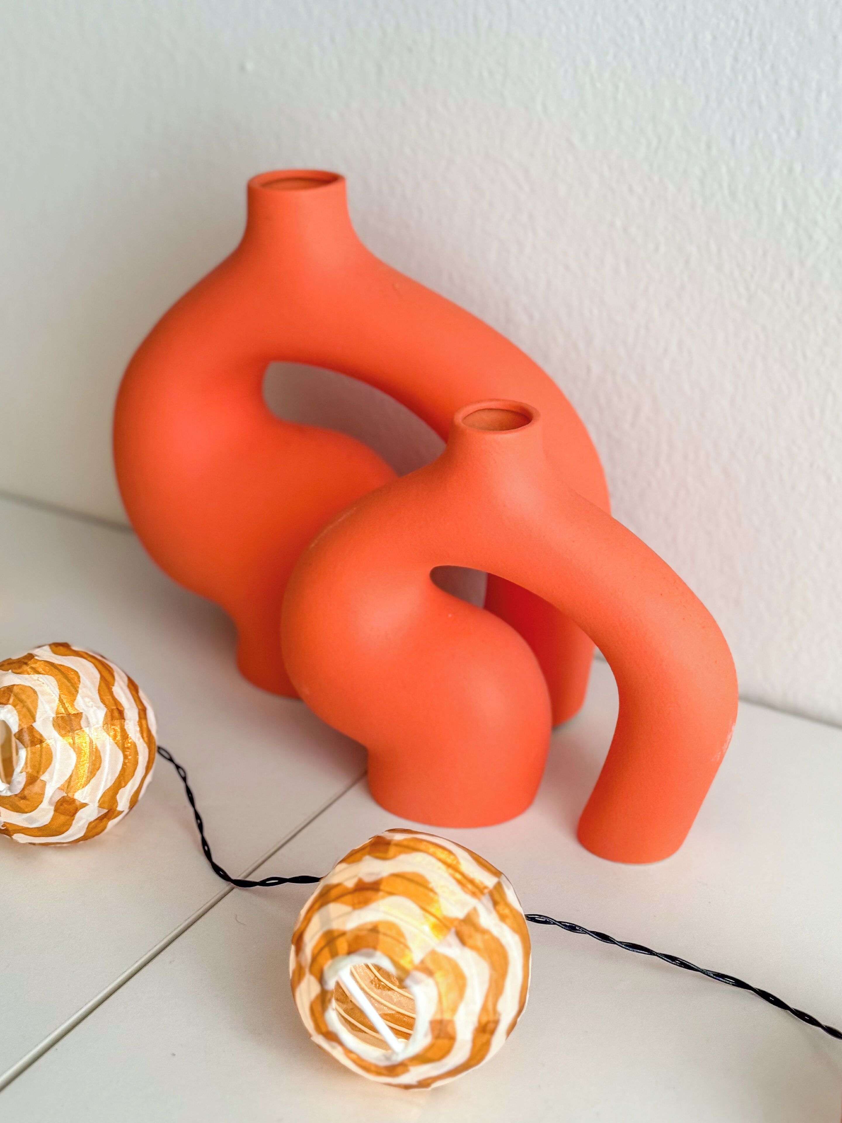 Two orange vases and two spherical ornaments on a white surface.