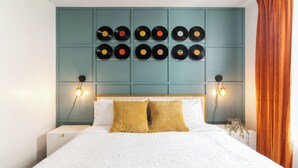 A neatly made bed with a white and blue bedspread, two mustard-colored pillows, and a teal headboard with vinyl records displayed. - 2-bedroom apt in Marina del Rey with pool, jacuzzi, gym, free parking! (Marina del Rey)