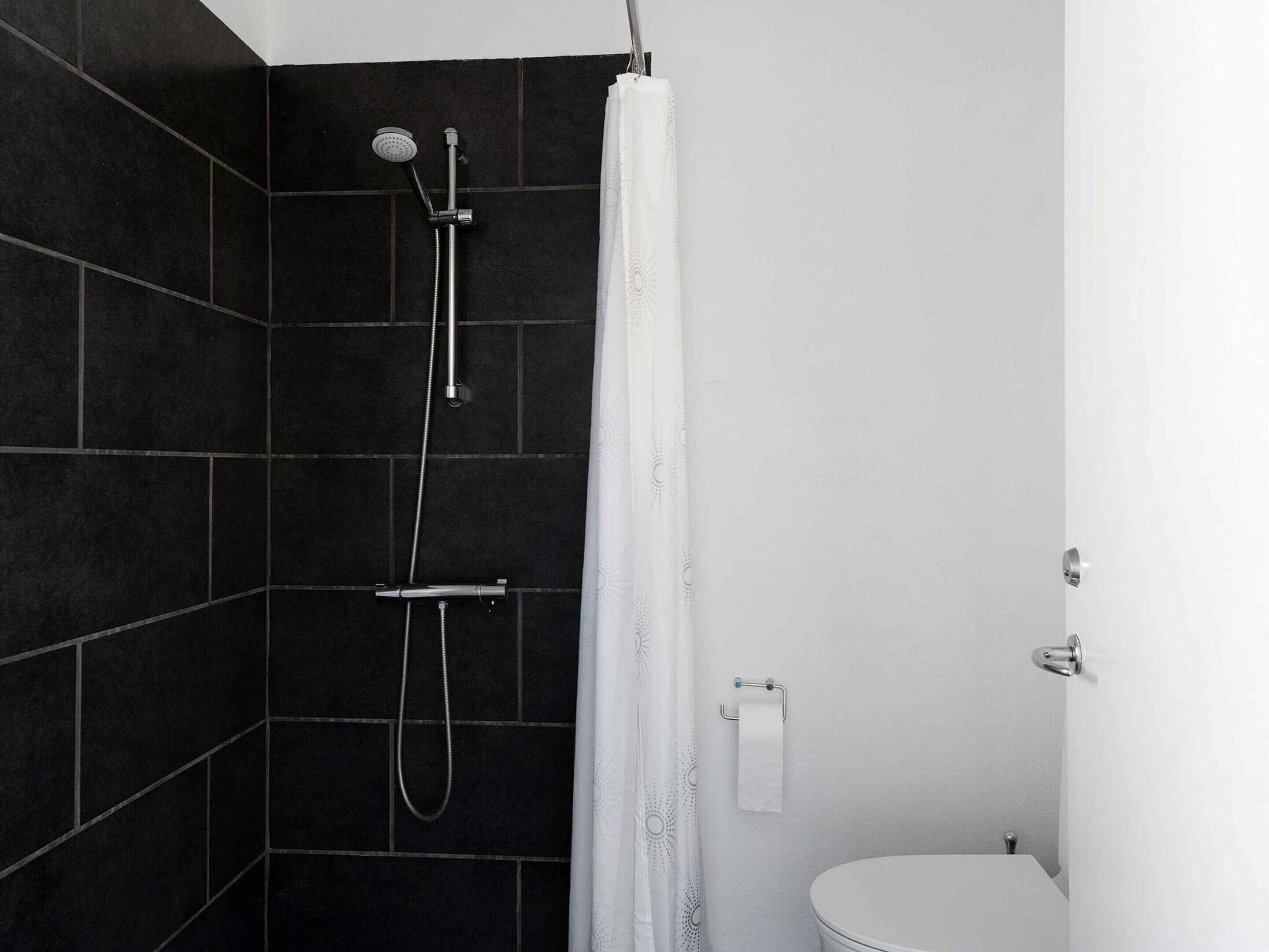 A modern bathroom with a shower, dark tiled walls, a white toilet, and a curtain.