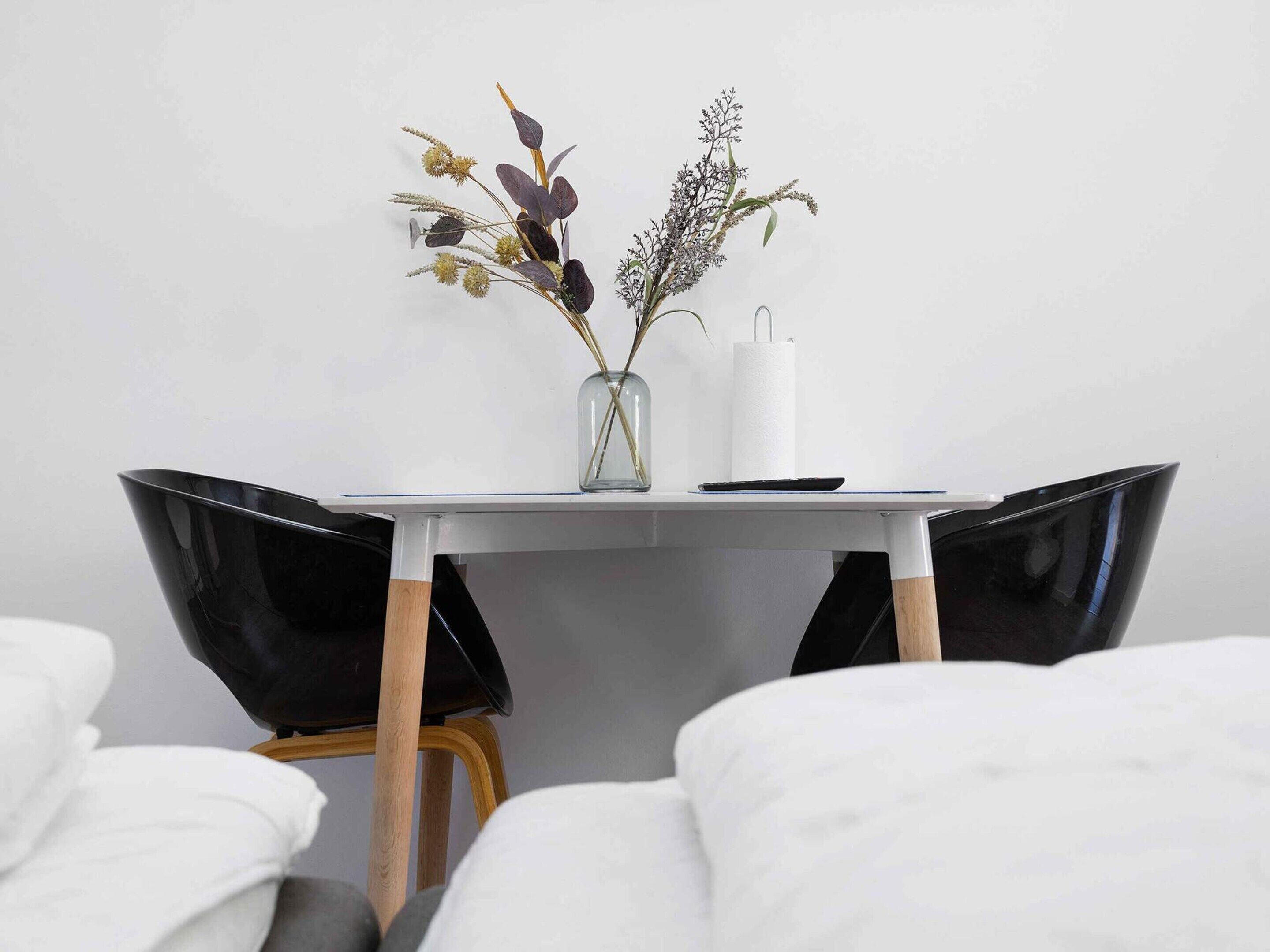 A dining table with a vase of dried flowers, a white napkin holder, and a black remote control.