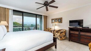 Una habitación de hotel con una cama grande, ventilador de techo, televisión, escritorio y una silla.