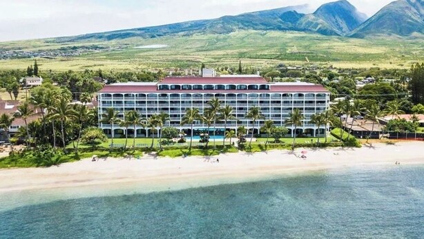 Un hotel con techo rojo, varios pisos y una zona de piscina.