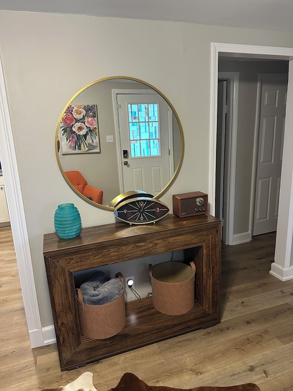 A wooden console table with a mirror, a clock, and two leather storage bins.