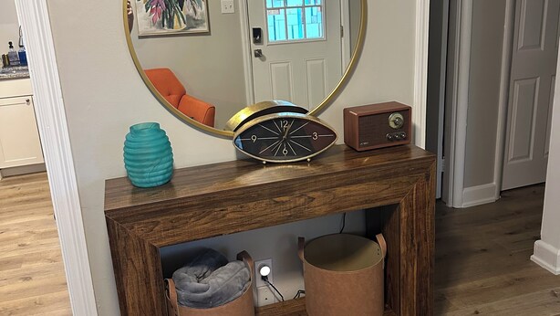 A wooden console table with a round mirror, a clock, and two leather poufs. - Livie’s Cozy Cottage Near Collierville (Olive Branch)