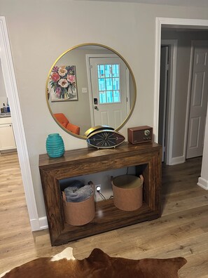 Une console en bois, ornée d’un miroir rond, d’une horloge et de deux poufs en cuir.