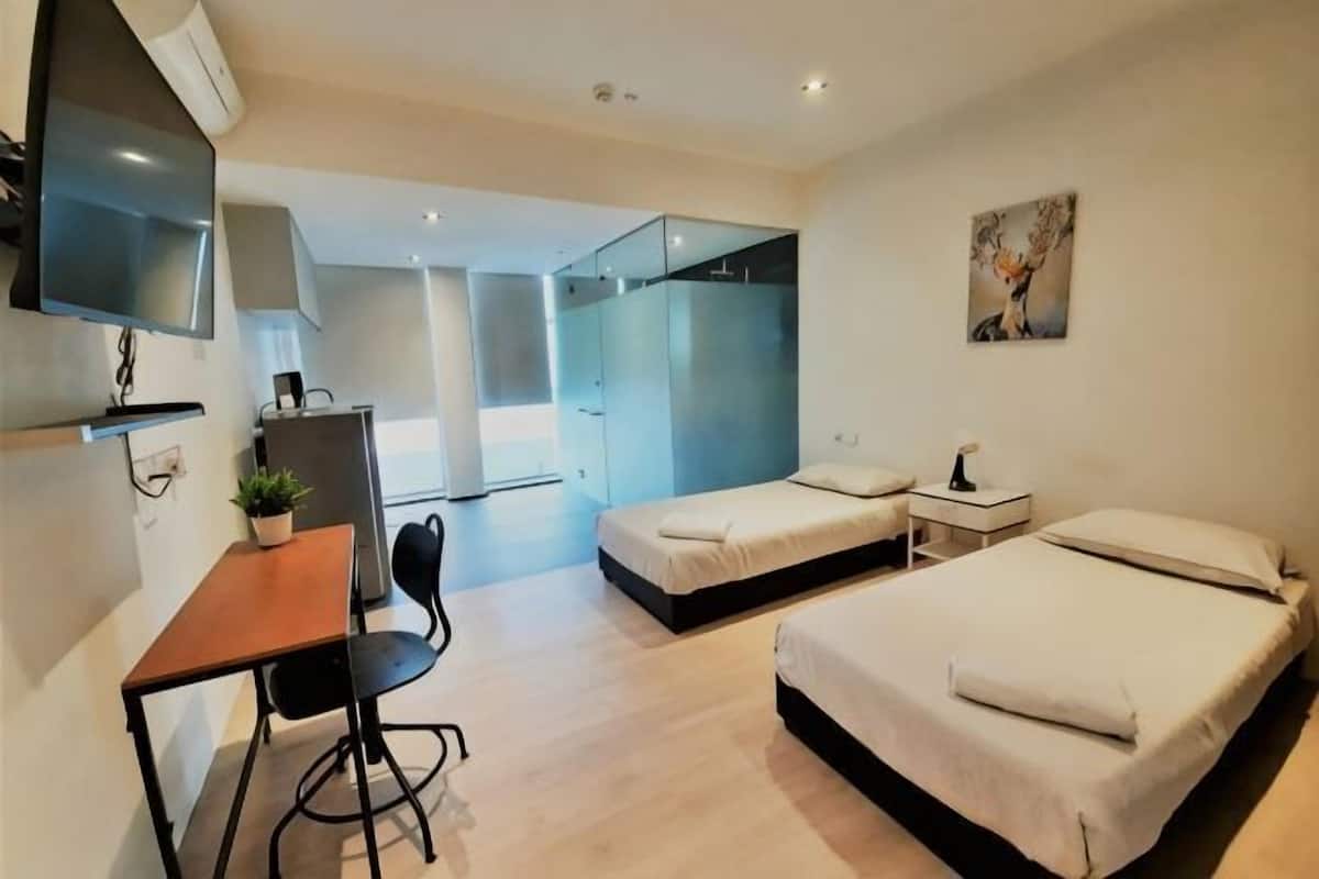 Une chambre d’hôtel moderne équipée d’un bureau, de deux lits, d’une télévision et d’une douche à parois de verre.