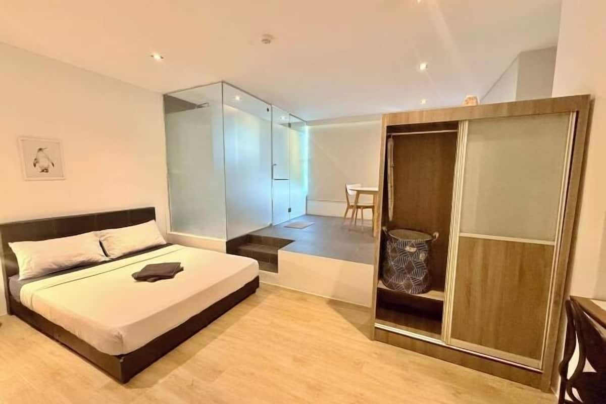 Une chambre à coucher moderne avec un lit, une cloison en verre, une armoire en bois et une petite table.