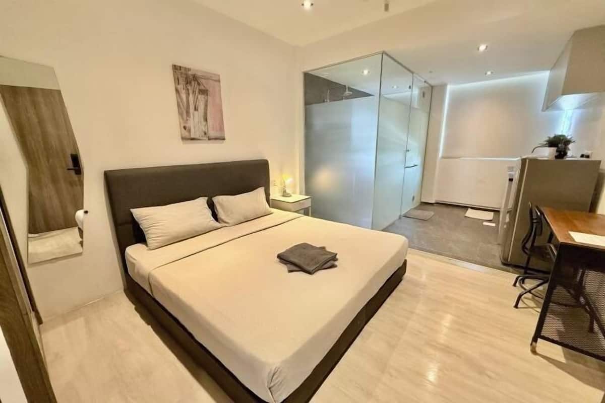 Une chambre moderne avec un lit, une table de chevet et une cloison en verre donnant accès à une salle de bain.