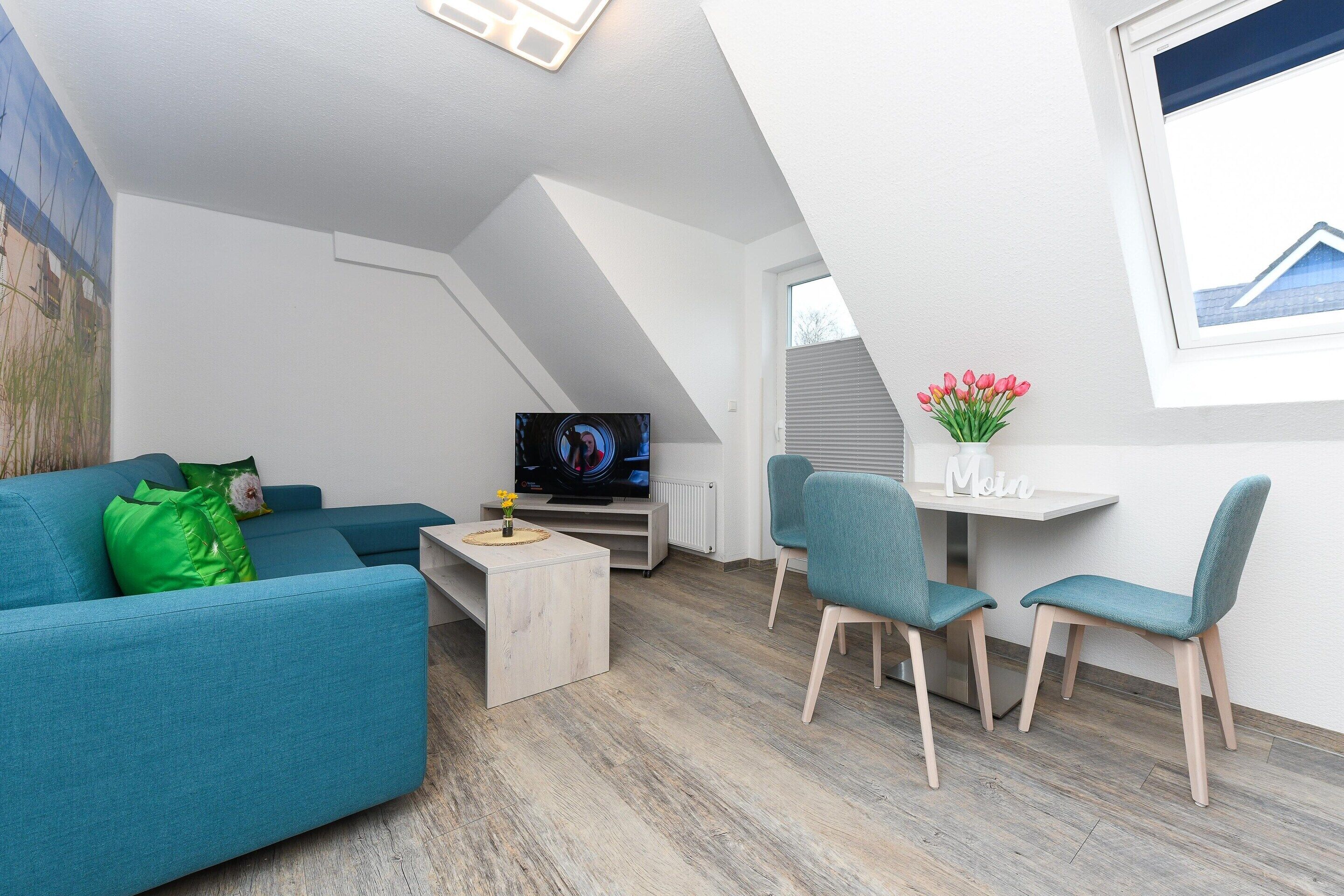 Una sala de estar moderna con un sofá, una mesa de centro, un televisor y un comedor con sillas y una pequeña mesa.