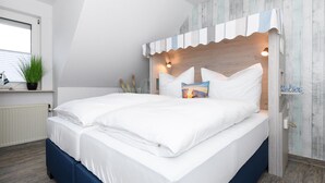A neatly made bed with white linens, a wooden headboard with a striped accent, and a small bedside table with a lamp. - Helle Ferienwohnung fur Zwei Personen in Bensersiel (Esens)
