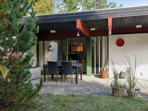 A modern outdoor patio with a dining table and chairs, a glass door leading to an interior space, and a brick wall with a red accent. - 4 Star Holiday Home in Hojby (Hojby)
