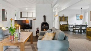 Un soggiorno moderno con camino, zona pranzo e cucina dalle pareti in mattoni bianchi e travi in legno.