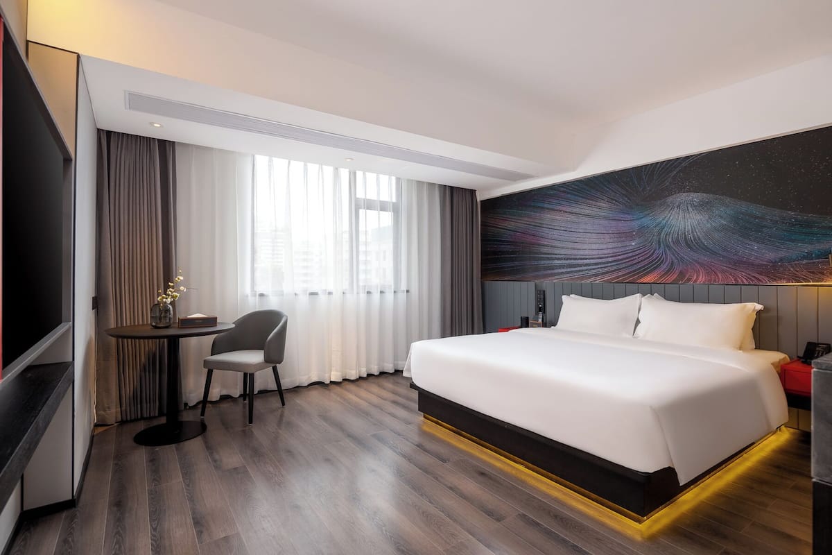 Une chambre d’hôtel moderne dotée d’un grand lit, d’un bureau avec une chaise, d’un téléviseur à écran plat et d’une grande fresque murale.