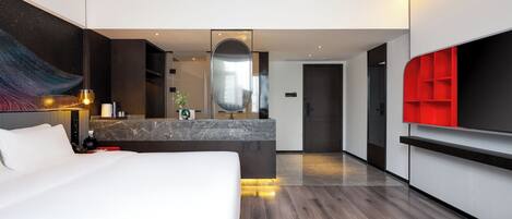 A modern hotel room with a large bed, a central island with a sink, a mirror, and a red accent wall.