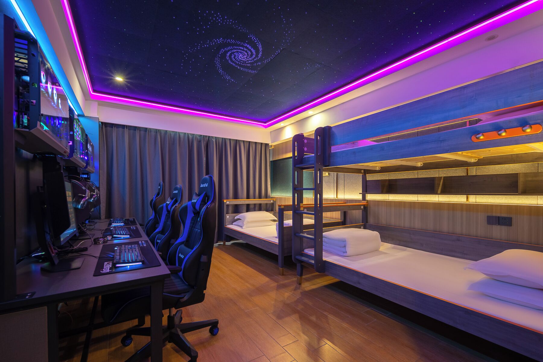 Quarto de hotel moderno com estação de jogos, beliches e design de teto com efeito de céu estrelado.