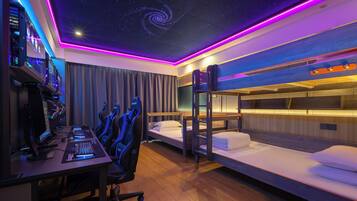 Quarto de hotel moderno com estação de jogos, beliches e design de teto com efeito de céu estrelado.