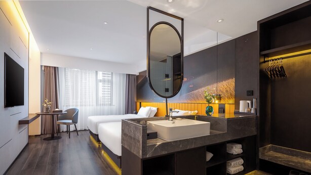A modern hotel room with a large bed, a desk, a bathroom with a large mirror, and a TV. - LiangZhi Huipin Hotel (Haikou)