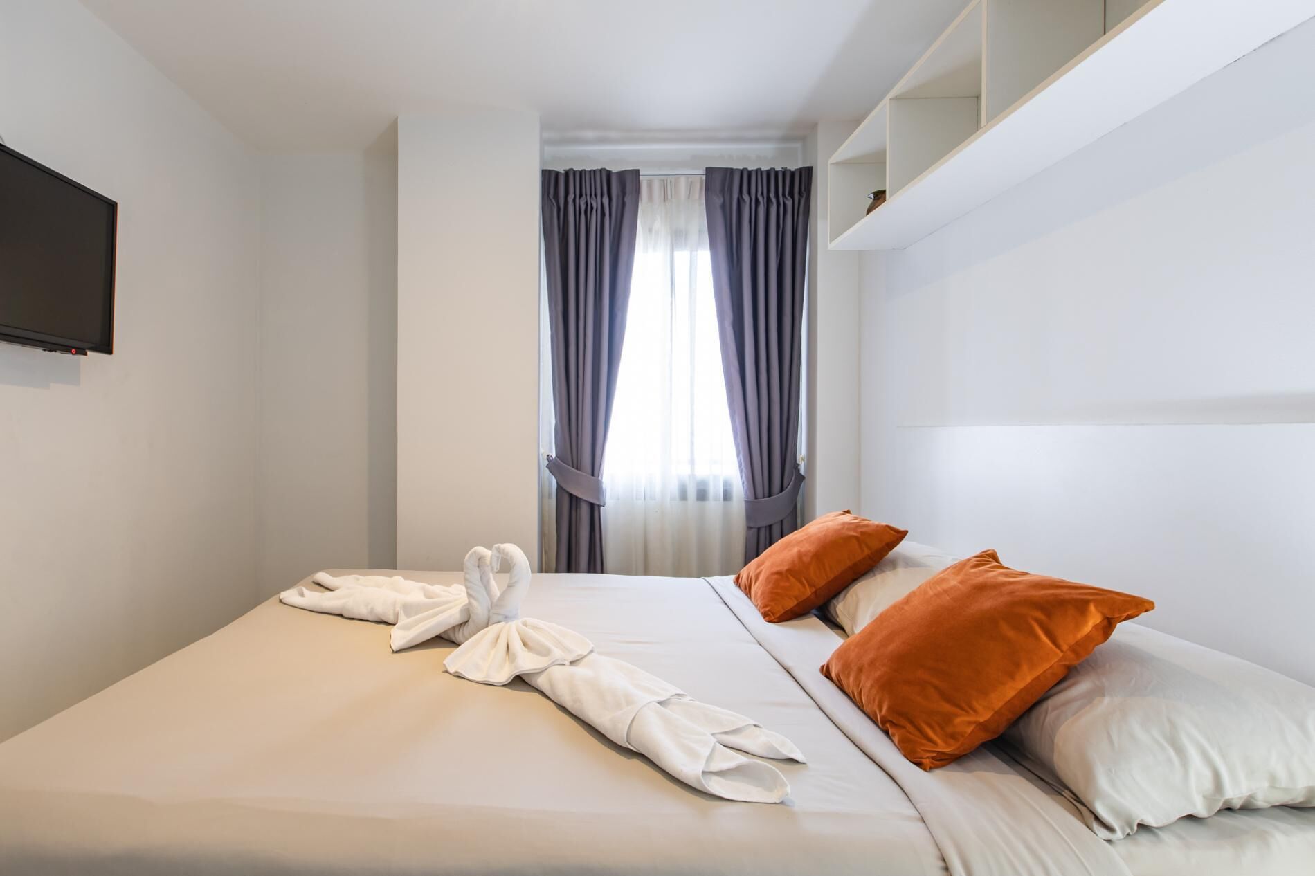 Siisti hotellihuone, jossa on huolitellusti pedattu sänky, seinälle asennettu taulutelevisio ja ikkuna, jossa on verhot.