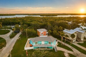 A coastal property with a large house featuring a balcony, surrounded by lush greenery and a view of the ocean.