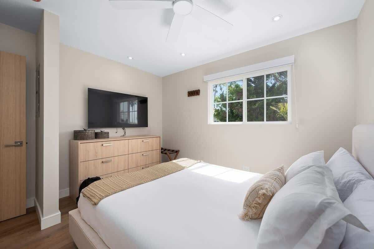 Ein Schlafzimmer mit Bett, Fernseher, Fenster und Deckenventilator.