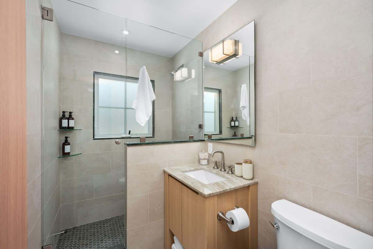Un baño moderno con cabina de ducha de vidrio, tocador de madera con lavamanos y un inodoro.