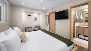 A hotel room with a bed, a TV, a desk, and a bathroom with a mirror and sink. - Modern 2BR Near Beach w/ Parking, Spa, BBQ, EV (San Diego)