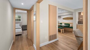 A modern interior with a wooden floor, a green sofa, a dining table, and a bed in the adjacent room. - Modern 2BR Near Beach w/ Parking, Spa, BBQ, EV (San Diego)